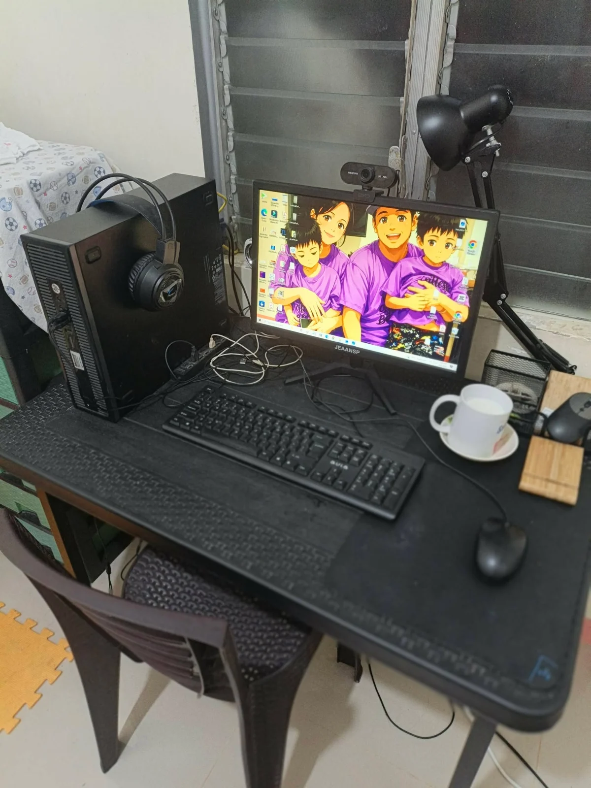 My desktop work setup by the window, with a webcam, headphones, and desk lamp
